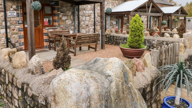 A rustic stone building with a wooden bench and a potted tree.
