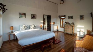 A spacious bedroom with a large bed, a wooden floor, a ceiling fan, and a dresser with decorative items. - Beyond Stay Jawai Legacy (Shivganj)