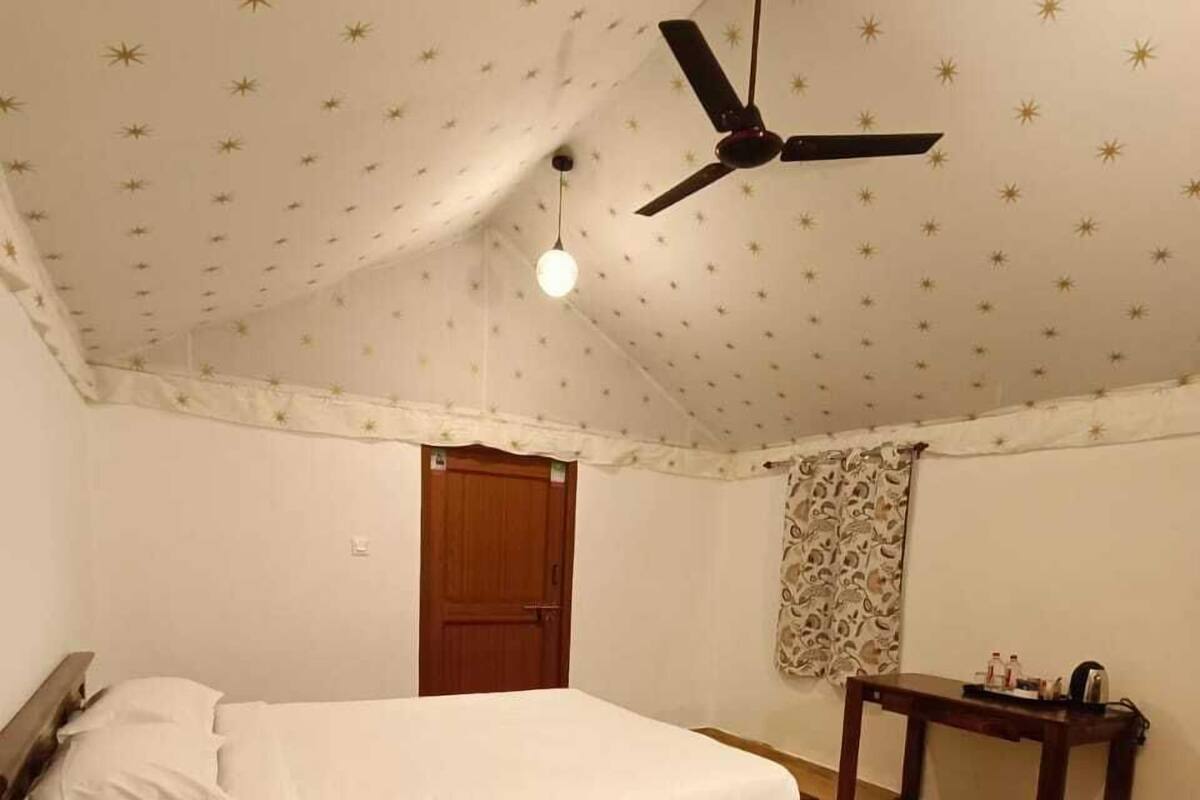 Un dormitorio con una cama, una mesa de madera, un ventilador de techo y un escritorio pequeño.