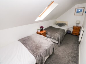 A small, tidy room with two beds, a wooden nightstand, a dresser, a radiator, and a skylight.