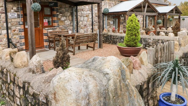 Un bâtiment rustique en pierre, avec un banc en bois et des plantes en pot.