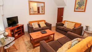 Un salon avec deux canapés, une table basse, un téléviseur posé sur un meuble en bois et un miroir accroché au mur.