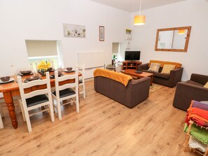 A living room with a dining area, wooden flooring, a sofa, a television, and a mirror.