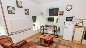 Ein gemütlicher Wohnbereich mit einer Couch, einem Esstisch mit Stühlen, einer kleinen Küchenzeile inklusive Kühlschrank, Mikrowelle und Wasserkocher.