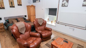 Ein Schlafzimmer mit einem Bett, zwei Ledersesseln, einem Holztisch und einem Fenster mit Blick nach draußen.