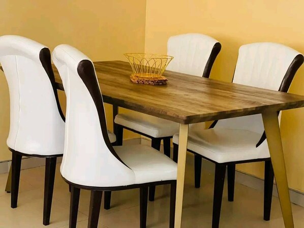 Una mesa de comedor con cuatro sillas blancas y una cesta de alambre sobre una superficie de madera.