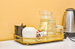 Una bandeja con una cafetera, una jarra de vidrio, una taza blanca y un jarro de vidrio sobre una mesa frente a una pared amarilla.