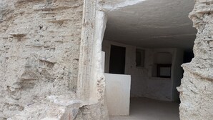 Un étroit passage aux murs de pierre brute, avec une porte donnant sur une pièce dotée d’une fenêtre et d’une autre porte.
