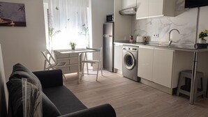 Un espace de vie compact comprenant un canapé, une table à manger, des chaises, un lave-linge, un réfrigérateur et une cuisine équipée d’un évier et d’une cuisinière.