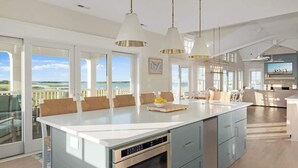 Una cocina amplia con una isla grande, elegantes lámparas colgantes y ventanas grandes que ofrecen vistas al exterior.