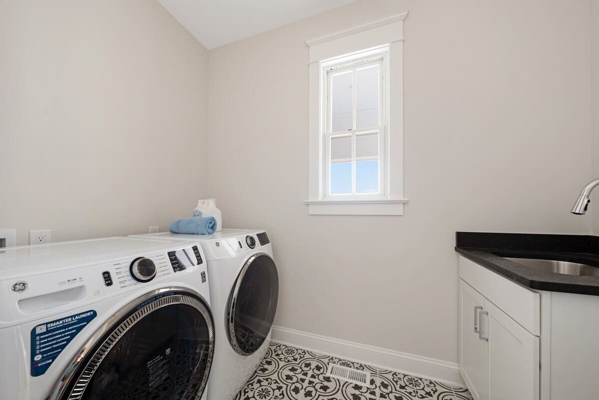 A laundry room with a front-loading washer and dryer, a window, and a sink.