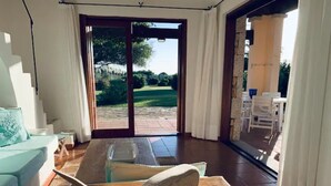 A modern living room with a wooden coffee table, a teal sofa, and a view of a garden through a glass door. - 3 bedroom villa in sardinia (Sardegna)