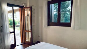 A bedroom with a bed, a window with a view of greenery, and a sliding glass door leading to an outdoor area. - 3 bedroom villa in sardinia (Sardegna)