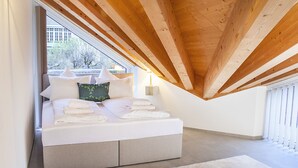 A bedroom with a sloped ceiling, a bed with white linens, a green pillow, and a nightstand with a lamp.