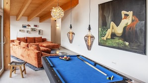 A cozy living room with a pool table, a sofa, and a painting on the wall.