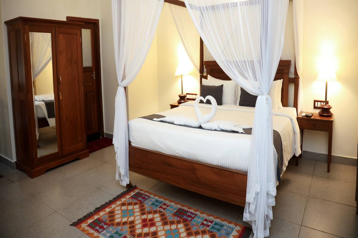A four-poster canopy bed with a mirror cabinet and bedside lamps.