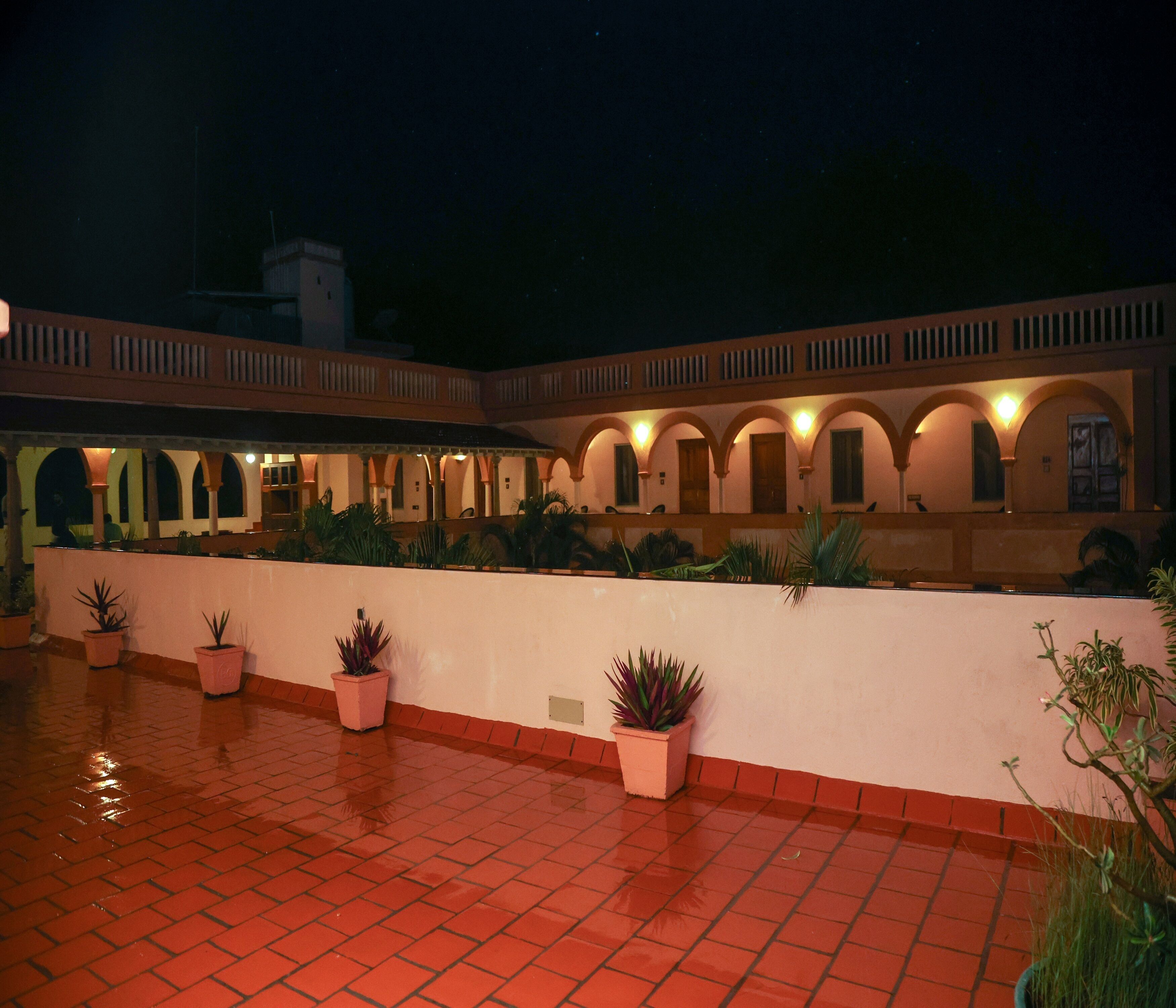 A courtyard with a tiled floor, potted plants, and a building with arched windows and balconies.