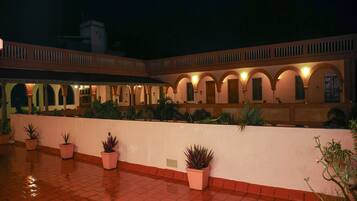 A courtyard with a tiled floor, potted plants, and a building with arched windows and balconies.