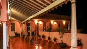Un espacio exterior techado con suelo de baldosas, columnas y plantas en macetas.
