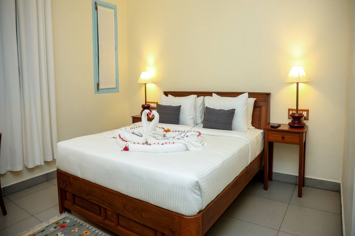 A neatly made bed with a decorative swan towel arrangement, two bedside lamps, and a wooden nightstand.
