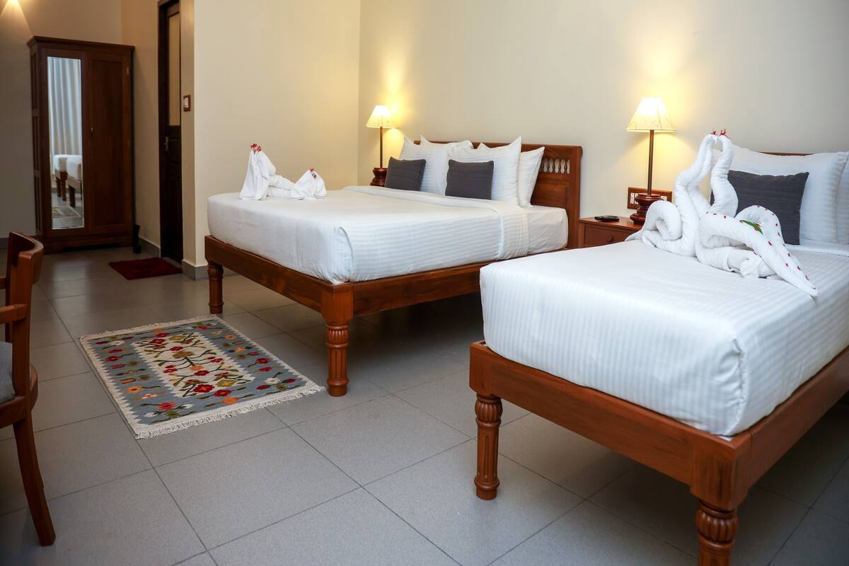 A hotel room with two wooden beds, a wooden chair, a small rug, and a door leading to another room.