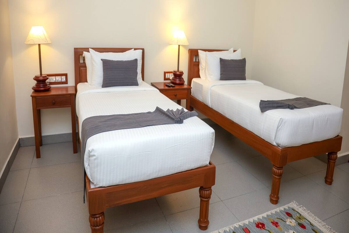 Two single beds with wooden frames and white linens, each with a bedside table and lamp.