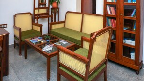 Una sala de estar con un sofá verde, sillas de madera, una mesa de centro y una estantería.