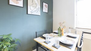 Een eethoek met een tafel gedekt voor twee personen, kunstwerken aan de muur en een potplant ernaast.