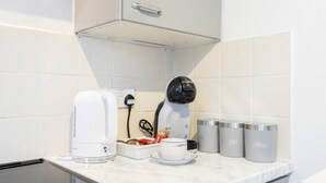 Een keukentafel met een koffiezetapparaat, een kop koffie en twee bakjes met de tekst 'thee' en 'suiker'.