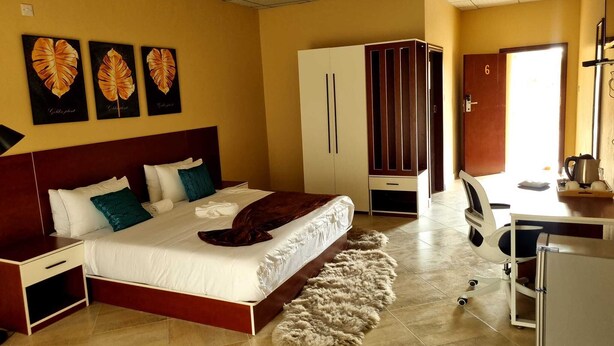 A hotel room with a bed, a wardrobe, a desk with a kettle, and a chair. - Eden Wood Guest House (Shakawe)