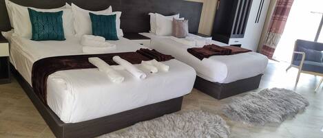 A hotel room with two beds, a large dark headboard, a grey furry rug, and a grey furry ottoman.