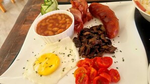 A plate with eggs, beans, bacon, mushrooms, and tomatoes. - Eden Wood Guest House (Shakawe)