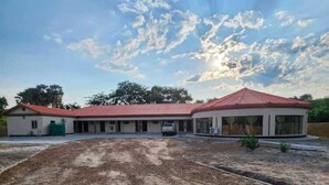 A building with a red roof and a large open area in front. - Eden Wood Guest House (Shakawe)