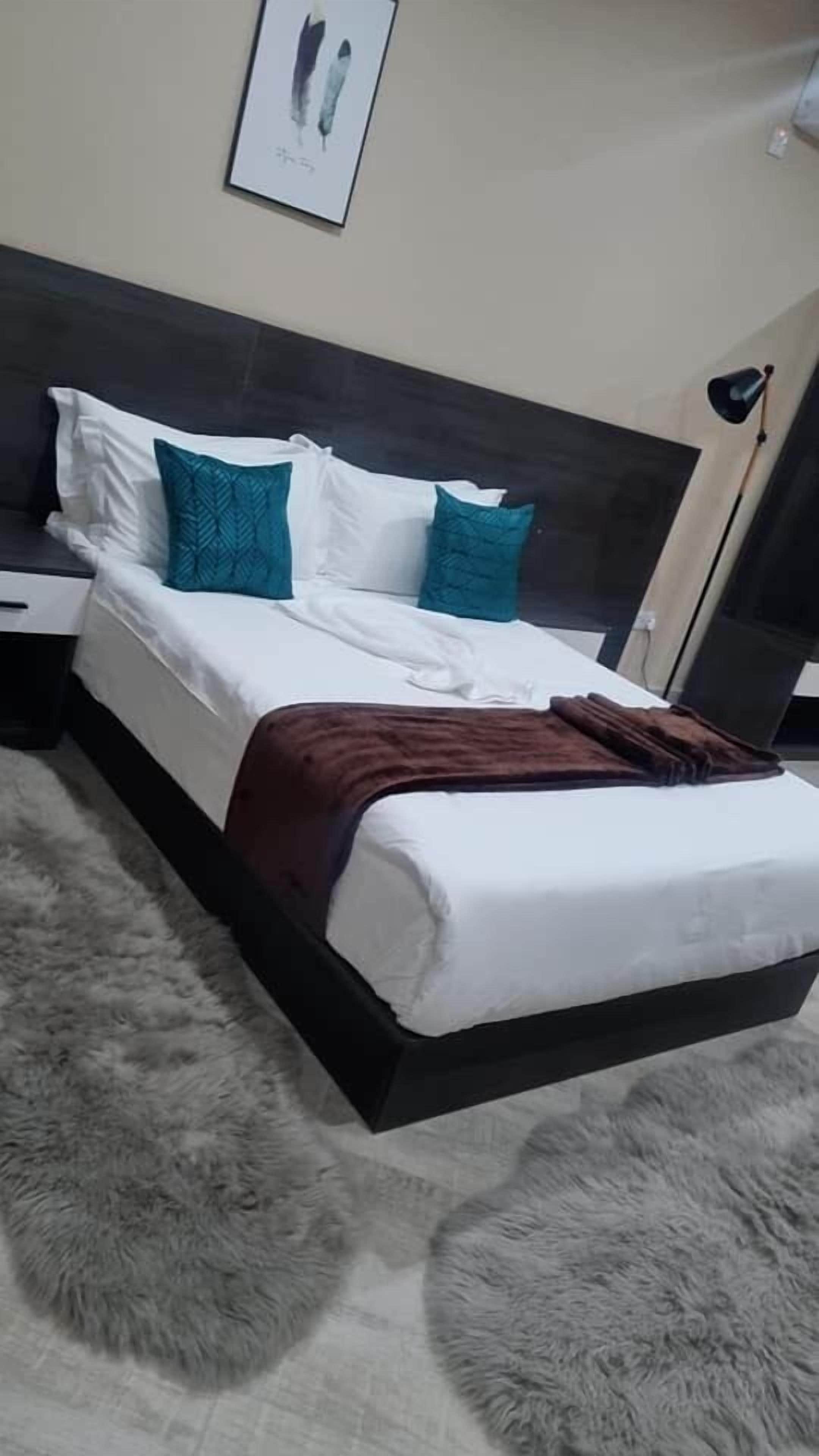 Una cama con ropa blanca, almohadas verde azulado y blanco, y una manta marrón.