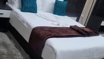 Una cama con ropa blanca, almohadas verde azulado y blanco, y una manta marrón.
