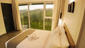 A hotel room with a large bed, a view of a forest through a sliding glass door, and a balcony.