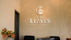 A reception desk with a logo for "The Leaves" hotel, a vase with flowers, and a Lenovo laptop.