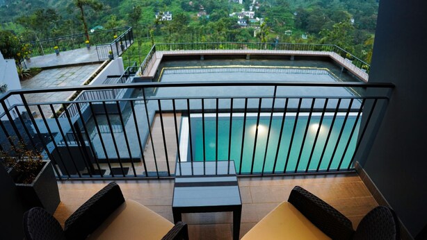 A balcony with a pool, wicker furniture, and a view of a lush landscape.