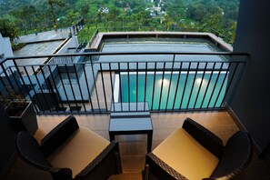 A balcony with a pool, wicker furniture, and a view of a lush landscape. - The Leaves Resort Vythiri (Vythiri)