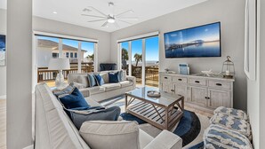 Ein geräumiges Wohnzimmer mit großem Fenster, Deckenventilator, Fernseher und Blick auf einen Steg und Wasser.