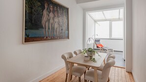 Een eetruimte met een tafel en stoelen, een schilderij aan de muur en uitzicht op de omgeving door een raam.