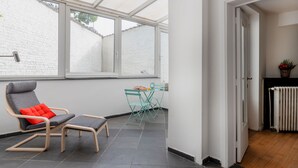 Een moderne kamer met een groot raam, een stoel met kussen, een klein tafeltje en een radiator.