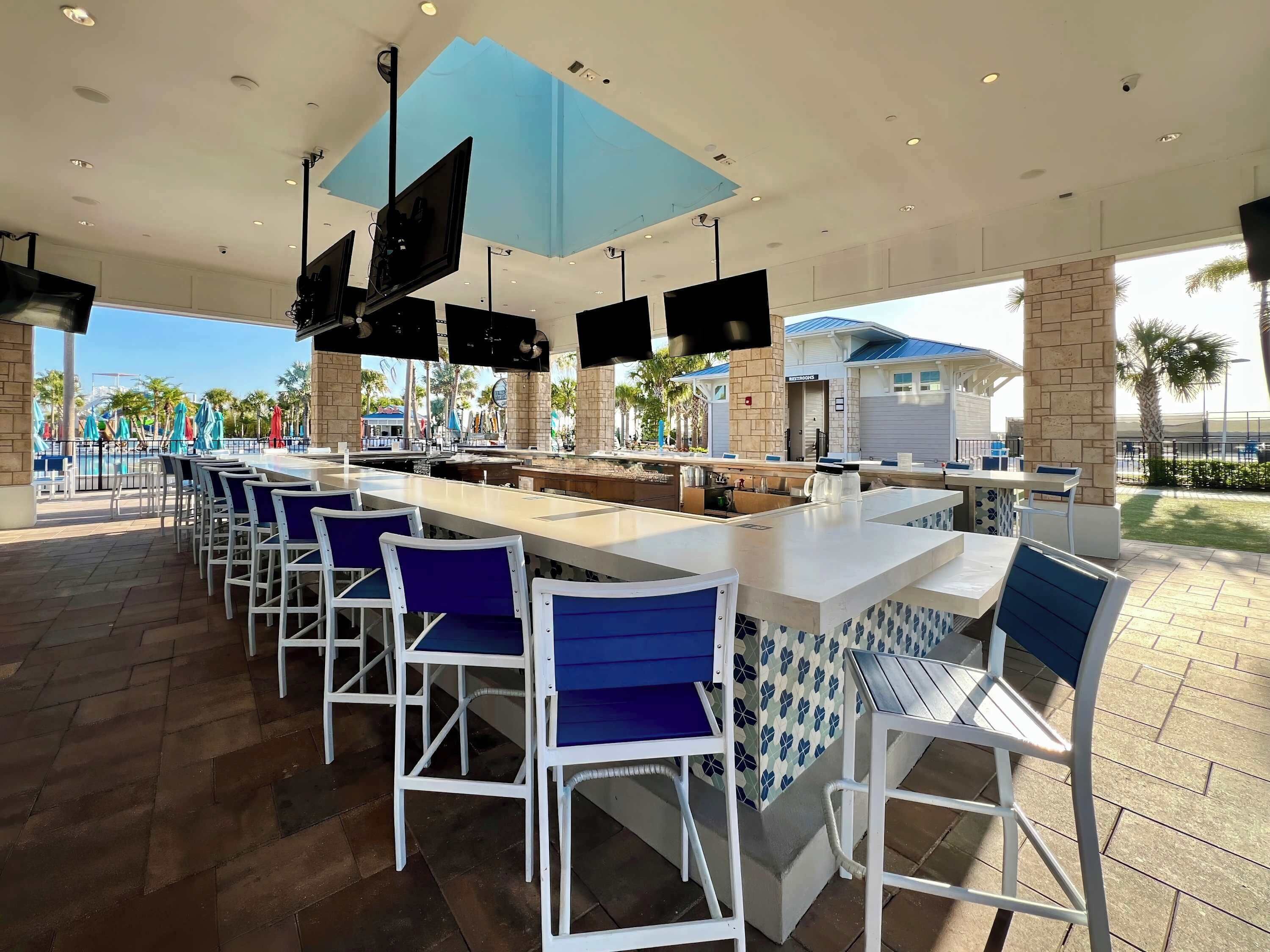A spacious outdoor bar area with multiple seating arrangements, a poolside view, and a modern architectural design.