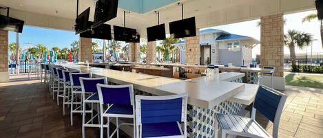 A spacious outdoor bar area with multiple seating arrangements, a poolside view, and a modern architectural design.