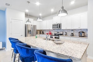 A modern kitchen with white cabinets, a granite countertop, and blue bar stools.