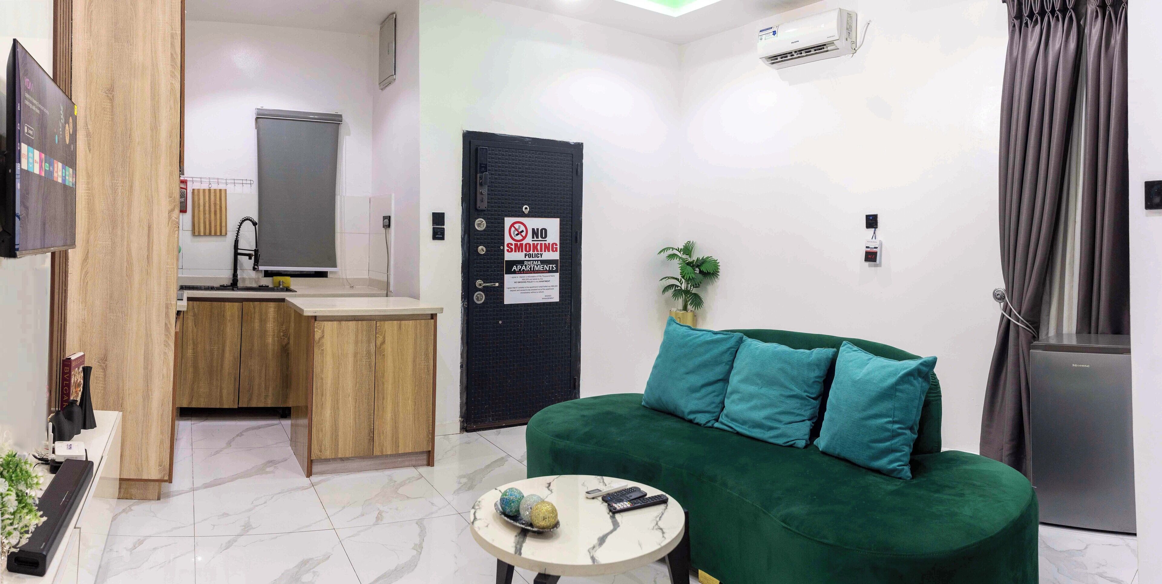 Uma sala de estar moderna com um sofá verde, uma mesinha redonda e uma área de cozinha com pia e armários.
