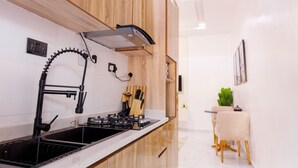 A modern kitchen with wooden cabinets, a black faucet, and a stove. - RHEMA APARTMENTS (Lagos)