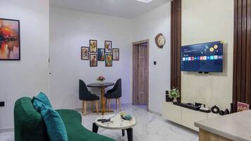 Una sala de estar moderna con un sofá verde, un comedor con dos sillas, una mesita y un televisor montado en la pared.