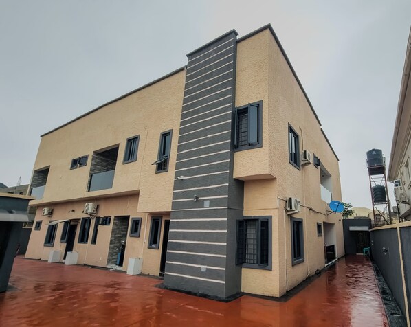 A multi-story building with a beige facade, black-framed windows, and air conditioning units. - RHEMA APARTMENTS (Lagos)
