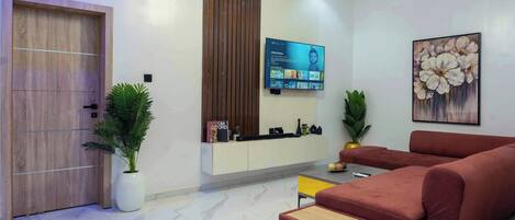 A modern living room with a red sofa, a TV mounted on the wall, and a potted plant.